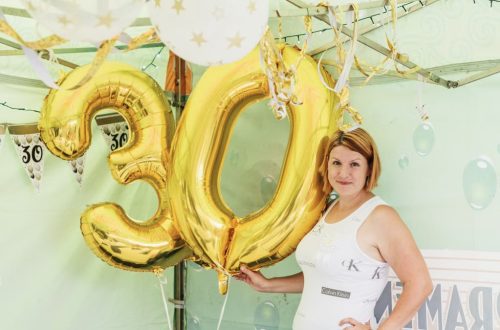 Woman posing with golden number 30 balloons at a birthday party celebration.