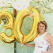 Woman posing with golden number 30 balloons at a birthday party celebration.