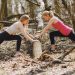 Side view of young female athletes in activewear stretching legs together using fallen tree during fitness workout in spring forest adhering to healthy lifestyle